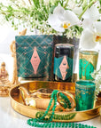 A luxurious setting features an elegant green and gold tea set on a gold tray, accompanied by a beaded green necklace, a small Buddha statue, and delicate white flowers in the background. The chic packaging suggests an artisanal product or gift set, perfect for enjoying Matcha 1111 : Highest Grade of Ceremonial Matcha by Magic Hour.