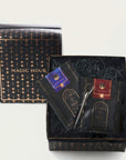 A gift box with a starry black design labeled "Magic Hour" on the lid contains two packets of luxurious loose leaf tea and a tea infuser. One packet is labeled "Blue Moon" and the other "Ruby Moon," both featuring elegant designs. The items are nestled in shredded black paper, making it the perfect Moon Lover: Herbal Immunitea Ritual Gift from Magic Hour.