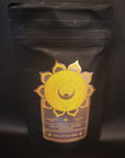 A black resealable pouch of Salutation™ Tea for the Solar Plexus Chakra is displayed against a dark background. The packaging features a golden geometric design with a sun motif and details "Solar Plexus Chakra Tea Blend - Salutation" in elegant gold text, highlighting its organic ingredients for optimal chakra balance.