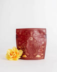The Year of the Rabbit Carrot Cake Tea comes in a red-brown resealable bag adorned with decorative gold designs, including two rabbits and celestial motifs representing the Chinese Zodiac sign. The bag stands upright, and to its left is a yellow flower with delicate petals, both set against a plain white background.