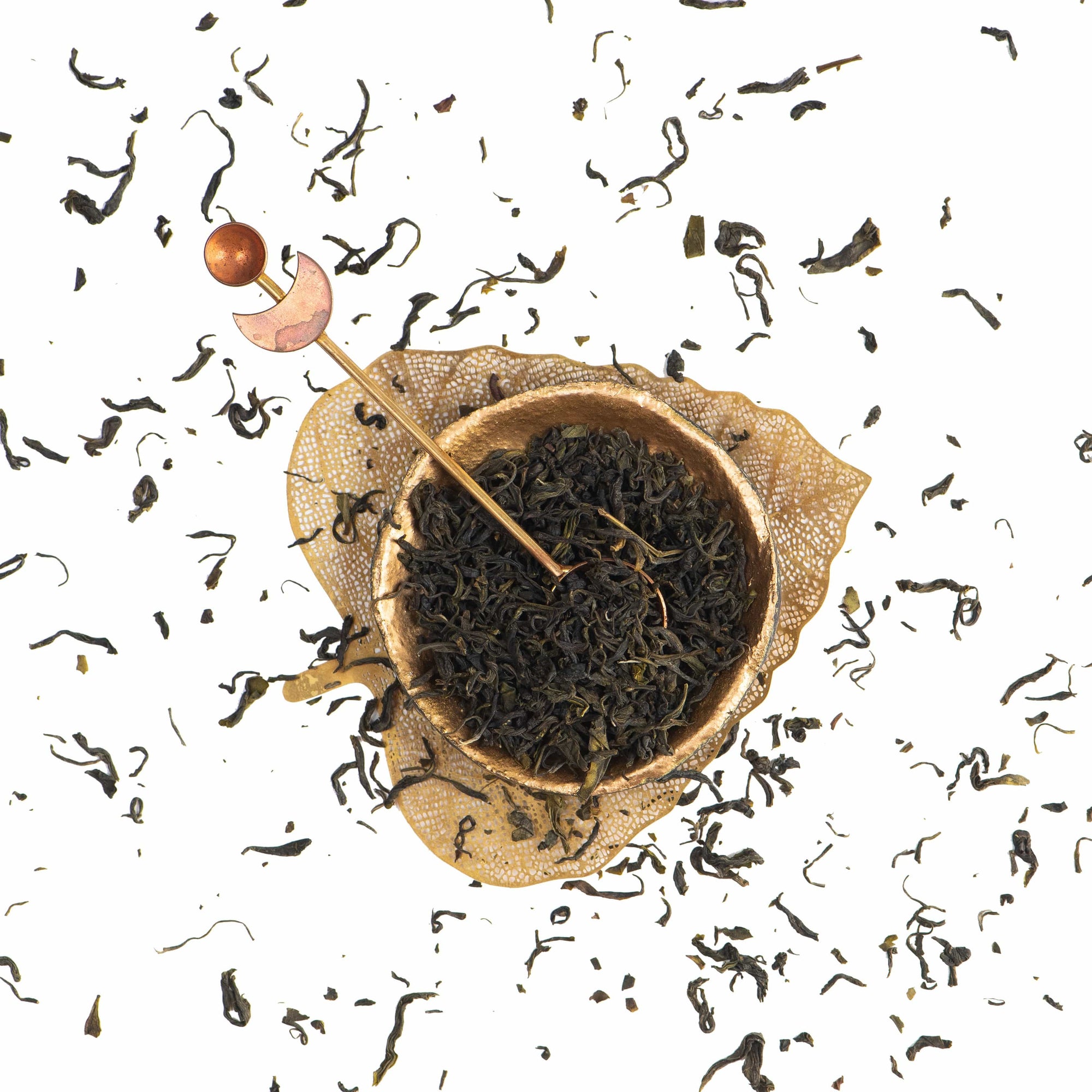 A bowl filled with Magic Hour Limited Edition Honey Black is placed on a piece of burlap. A decorative wooden scoop rests in the bowl, ready for your next cup. Loose tea leaves are scattered around the bowl on a white surface, inviting you to enjoy your own magic hour tea ritual.