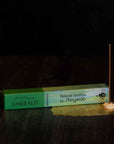 A Magic Hour natural incense stick named "Renew & Relax: Ritual Gift for Mindfulness & Calm" is lit and standing on a small holder. The incense packaging, green like Magic Hour Tea, rests on a dark surface. A delicate golden mesh is placed underneath the incense holder, creating an aura of tranquility and elegance.