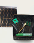 A black box labeled "Renew & Relax: Ritual Gift for Mindfulness & Calm by Magic Hour" is open, revealing its contents. Inside are two black packages with green labels and a gold metallic spoon. Another green box labeled "Emerald Natural Incense by Shoyeido" lies beside the packages inside the box, creating a serene setting for your organic tea experience.