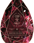 An image of a tea package designed to resemble a faceted garnet gemstone. The striking stand-alone gold foil front jar label, identified as "Magic Hour Front Jar Label," features the text "Time for Infinity, Ceremonial Teas, Made with Love, Gemstone Wellness Tea, Garnet" and includes a drawing of a teacup on a stand adorned with stars.
