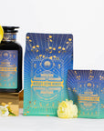 The image showcases a collection of three products labeled "Mercury Mint Nighttime: Vanilla Mint Lavender Jasmine Tea- Caffeine Free!" One item is a dark glass bottle with a gold-trimmed cap, another is a standing pouch, and the third is a small box, all adorned with a starry blue and green design. Arranged beside them are yellow and white flowers, highlighting the caffeine-free herbal blend featuring peppermint, vanilla mint, lavender, and jasmine.