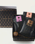 A gift box labeled "Sip Magic: Signature Blends of Magic Hour Ritual Gift" by Magic Hour contains three packages of black loose leaf tea with colorful labels: pink, brown, and copper. A tea infuser is also included. The packaging, adorned with a gold star pattern, adds an enchanting touch against the plain white background.