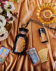 An elegant display featuring tarot cards, a black and gold bottle, glasses, a fan, and a floral arrangement on a silky, golden fabric. The tarot cards are arranged around the bottle, lending a mystical and luxurious ambiance to the setting—perfect for cozy sips of Magic Hour's Topaz - Caramel Apple Oolong Tea from the case packs.