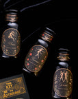 Three black bottles labeled "Pluto," "Sirius," and "Gemini" with elegant gold and floral designs are arranged on a black velvet surface. Next to them is a dark green book titled "The Key to Astrology" with gold lettering, perfect for sipping Magic Hour's Astrology Bundle: Aries, Taurus, Gemini - Magic Hour while you read.