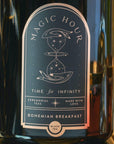Close-up of the Magic Hour Front Jar Label. At the top, the label reads "Magic Hour." Below, an hourglass image with a celestial design surrounds the text "Time for Infinity." The gold foil label also features "Ceremonial Teas" and "Made with Love," with "Bohemian Breakfast" at the bottom.