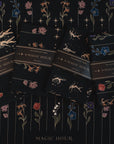 Four black tea towels, each with whimsical floral and star designs, are neatly laid out in a row. The towels are labeled "Tea Ceremony Towels Bundle" and are set against a matching background adorned with colorful flowers and celestial patterns, capturing the enchanting spirit of Magic Hour.