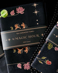 A close-up of the Tea Ceremony Towels Bundle by Magic Hour with floral and star patterns in gold and colorful designs. One towel is partially unwrapped, revealing its delicate design. Perfect for any Magic Hour Tea ritual, the packaging reads "TEA CEREMONY TOWELS BUNDLE by MAGIC HOUR 100% Cotton.
