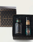 A gift box set labeled "Tea Connoisseur Collection" from Magic Hour contains three items. One is a candle in a black jar with gold accents, another is a small cylindrical container of loose leaf tea with a black lid, and the third item is similar in shape with a part-green, geometric design.