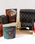 An arrangement of Magic Hour products featuring colorful packages with starry designs and a large black box adorned with gold stars. A small gold tea strainer and a brass tray are also part of the display, highlighting the elegance of their organic loose leaf tea offerings, including The Queen's Sampler Set.