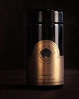 A black and gold tin with the label "Blissful Black Teas Medley" and "Magic Hour." The design features a circular logo and the words "Time ∞ Infinity." The container has a sleek, reflective surface and appears elegant against a dark background, ideal for showcasing premium loose leaf tea.