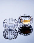 Two ribbed, transparent glass bowls sit on a reflective surface. One is empty, while the other, reminiscent of the Double-Walled Rippled Tea Cup, is half-filled with a golden liquid. The reflection of the bowls is visible beneath them.