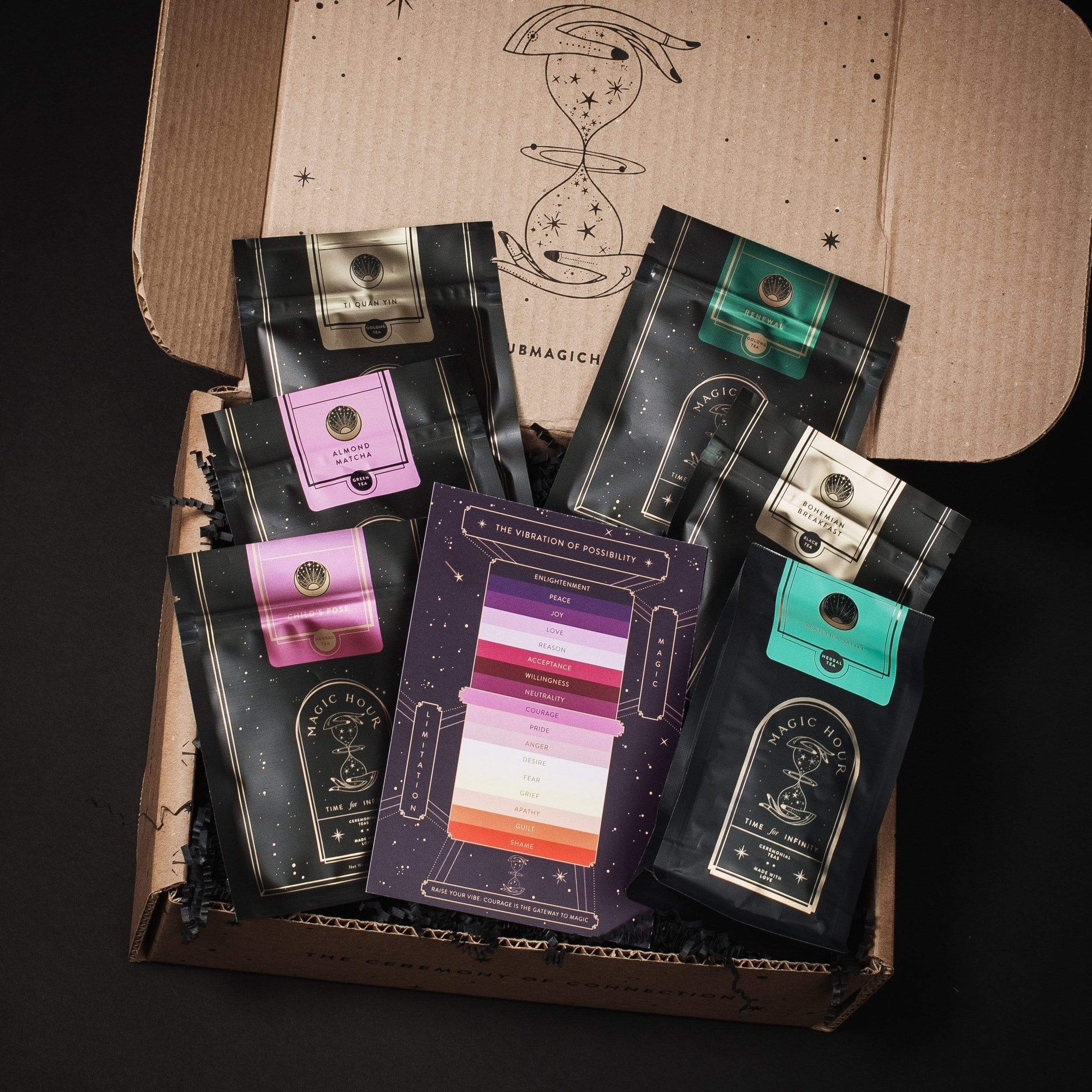 An open cardboard box reveals five bags of Self-Guided 14 Day Ceremonial Sensory Tea Cleanse Kits from Club Magic Hour, each in different colors: pink, green, gold, purple, and teal. In the center is a colorful card labeled "The Spectrum of Possibility" showing various flavor profiles. The interior has starry illustrations reminiscent of a Magic Hour Tea set.