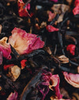 Close-up of a colorful blend of Soulmate: Chocolate-Raspberry-Rose Black Tea Traveler, featuring dried tea leaves and flower petals. The mixture includes dark loose leaf tea interspersed with vibrant pink, red, and purple petals, creating a visually rich and textured composition.