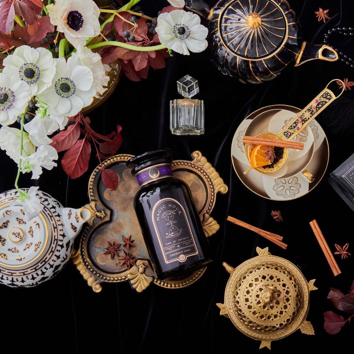 Arranged tea set with bottle, flowers, and decorative items on a satin cloth.
