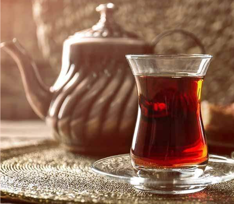 Glass tea cup of black tea with teapot in the background