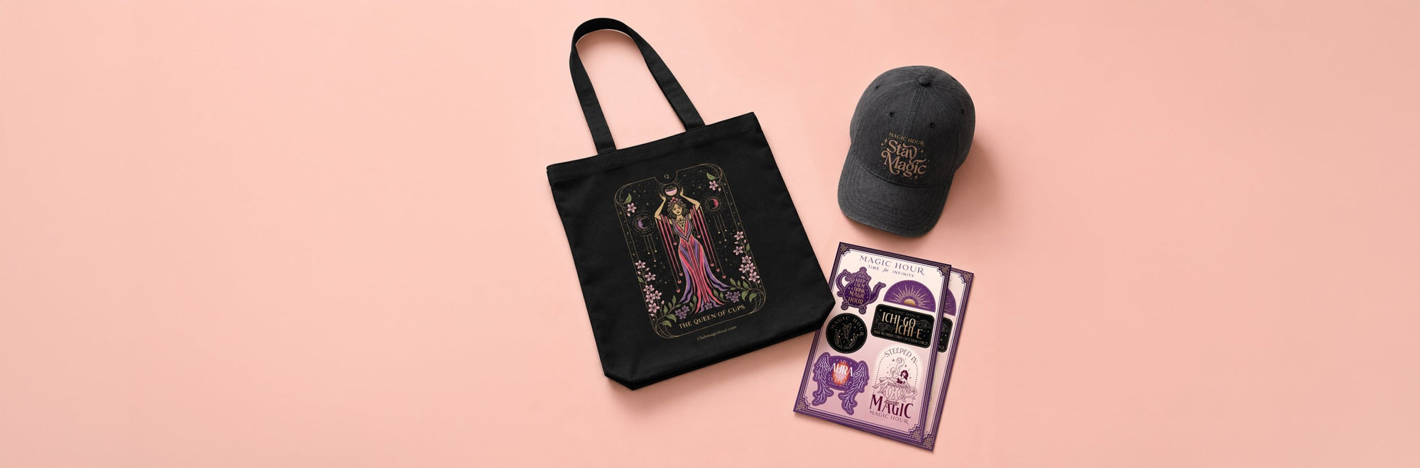 A black tote bag, a dark gray cap, two art prints, and several stickers with a magical theme, displayed on a pale pink background.