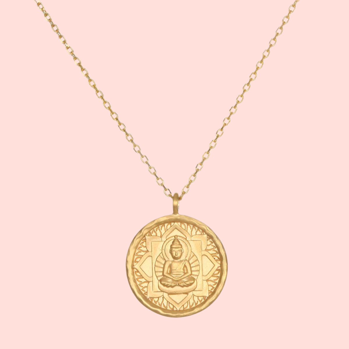 The Gold Buddha Pendant Necklace features a round pendant engraved with a seated Buddha at the center, framed by a decorative border. Finished in 18kt gold plate, it hangs from a delicate chain for an elegant look.