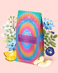 A vibrant tea package labeled “111: Lavender-Jasmine-Pineapple Herbal Tea with Blue Lotus” is surrounded by white and blue flowers, apple slices, and pineapple pieces—all on a soft pink background.