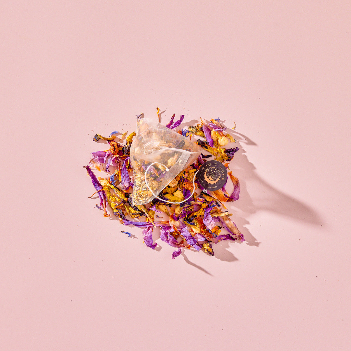 A Tea for Intuition: 1111: Pineapple & Butterfly Pea Flower Herbal Tea pyramid sachet resting on a loose pile of dried butterfly pea flower petals, yellow blossoms, and fruit pieces.