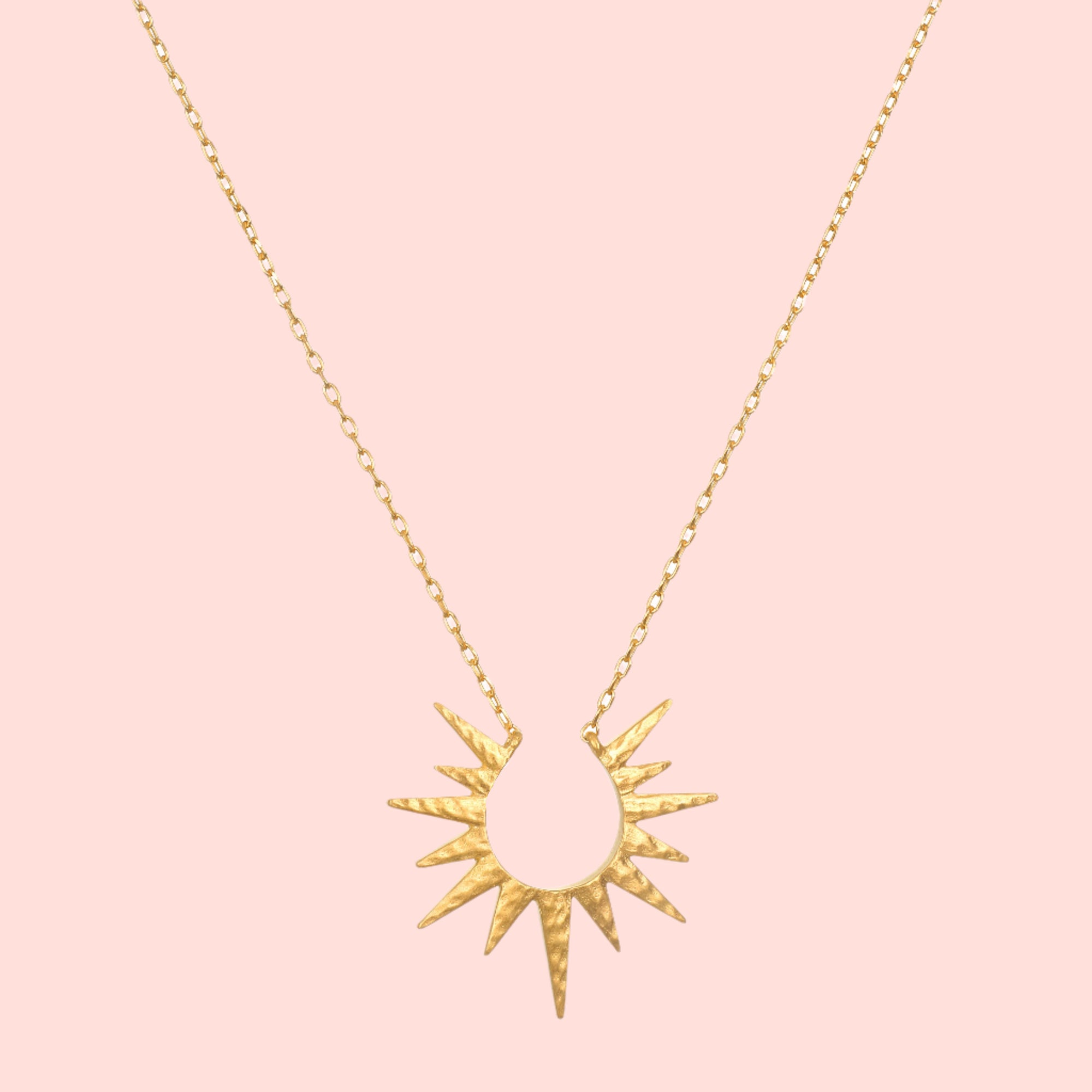 The 16" North Star Burst Necklace features a delicate chain and a sunburst-shaped pendant with pointed rays radiating from a central teardrop, all finished in textured, hammered 18kt gold plate for added charm.