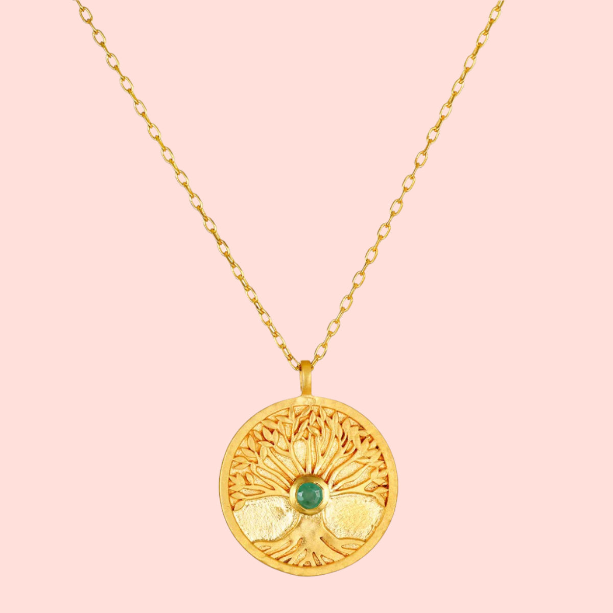 The Abundant Grounding Tree Necklace features a round gold pendant with intricate branches and a central emerald, all hanging elegantly from a delicate gold chain.