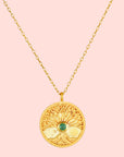 The Abundant Grounding Tree Necklace features a round gold pendant with intricate branches and a central emerald, all hanging elegantly from a delicate gold chain.