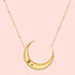 The Satya Jewelry Eternal Guidance Moon Necklace features a gold-plated crescent moon with two small dark pyrite stones on the lower left, hanging from a delicate beaded gold chain.