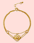 The Transformed by Love Lotus Bracelet is an 18k gold piece with a central lotus flower and a pink gemstone, flanked by two smaller pink stones and an adjustable clasp—ideal for lotus jewelry lovers.