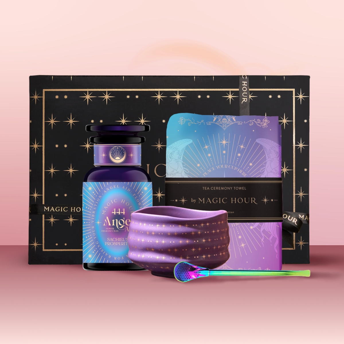 The Angel Numerology Fruit &amp; Flower Tea Gift Set includes a black and gold box, a blue and purple &quot;444 Angel&quot; tea jar, a matching tea towel, purple ceramic bowl, and decorative spoon, elegantly displayed on a pink background.