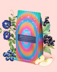 A vibrant tea package labeled "444: Sachiel's Prosperity" sits among blueberries, apple slices, black elderberries, and blue flowers—an eye-catching blue elixir of apple-berry herbal tea with butterfly pea flower and blue spirulina.
