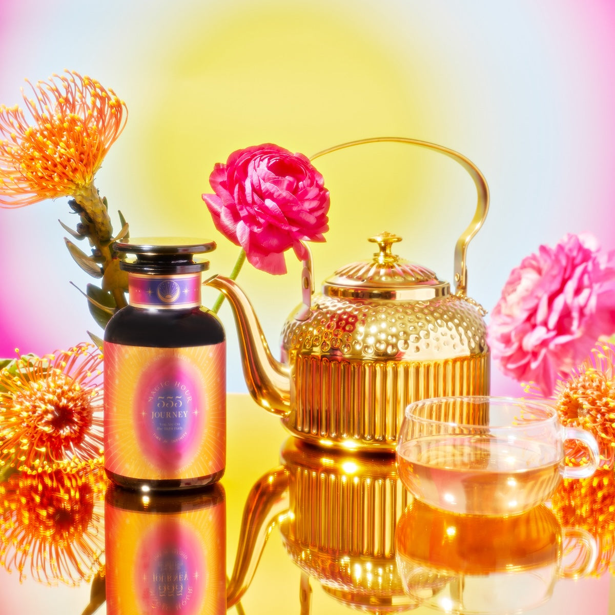 A vibrant scene features the School of Magic Tea Subscription Box in a golden teapot and glass teacup, hinting at mindfulness. Nearby, a jar with a gradient pink and orange label is surrounded by bright red and orange flowers, all reflected on a glossy surface against a colorful background.