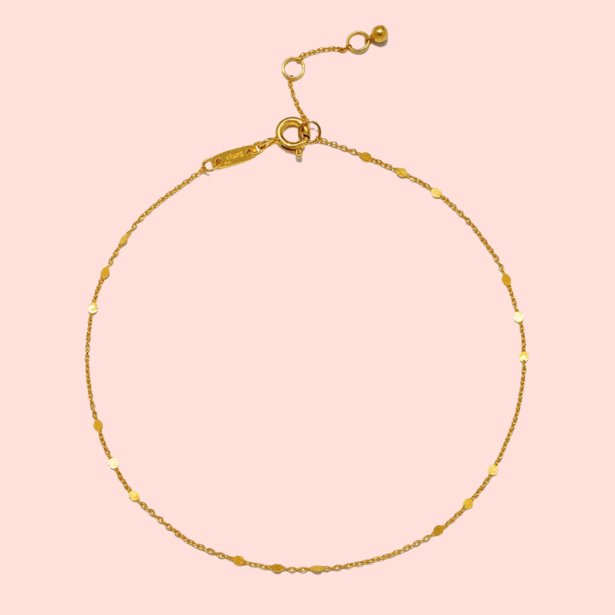 The 9" Shimmering chain anklet + 1" extender chain features delicate 18kt gold plating, tiny textured beads spaced along a shimmering chain, an adjustable clasp, and a small circular charm at the end.