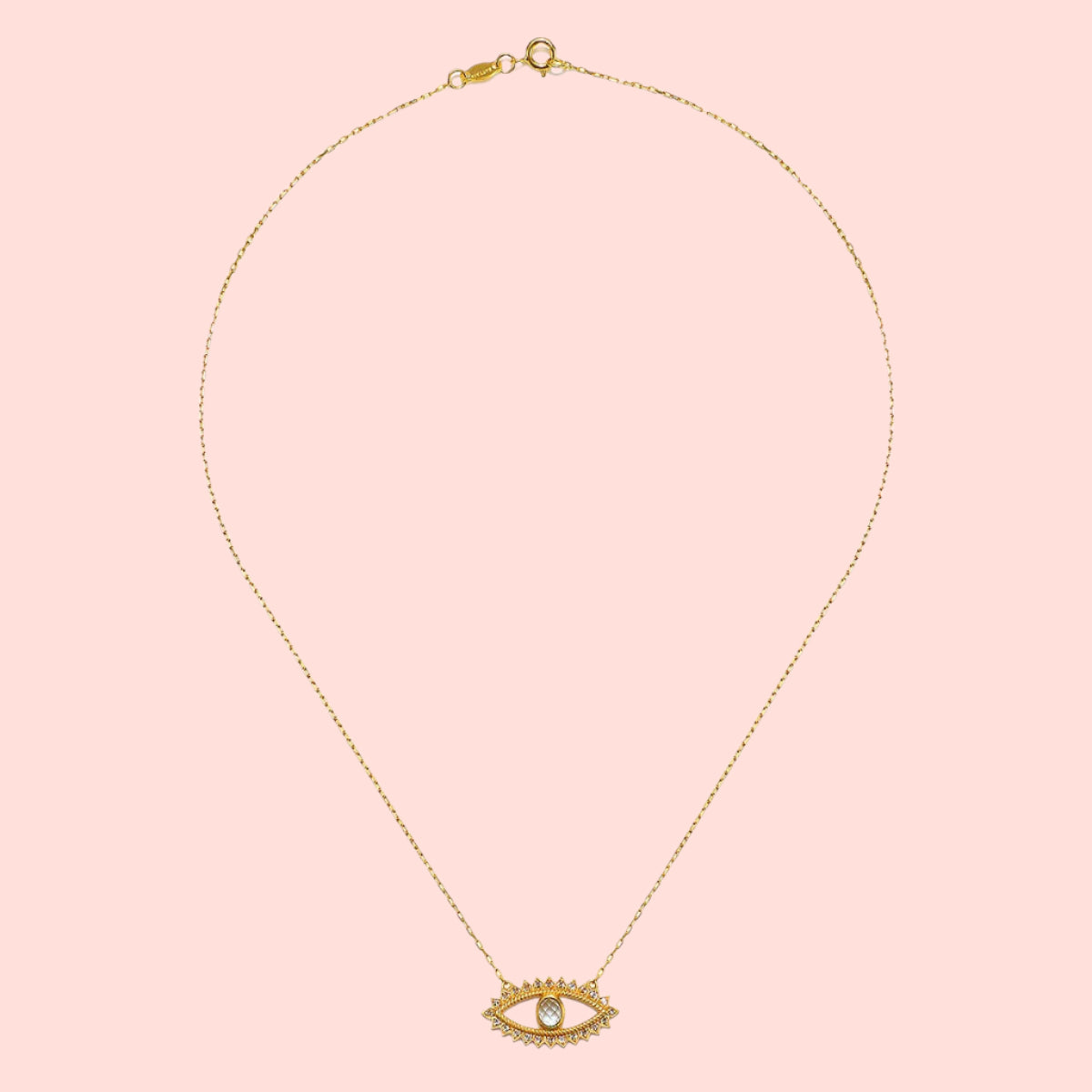 The Eye Blue Topaz Necklace is a gold-plated piece with an eye-shaped pendant, outlined with small clear stones and a larger blue topaz at the center, shown on a plain white background.