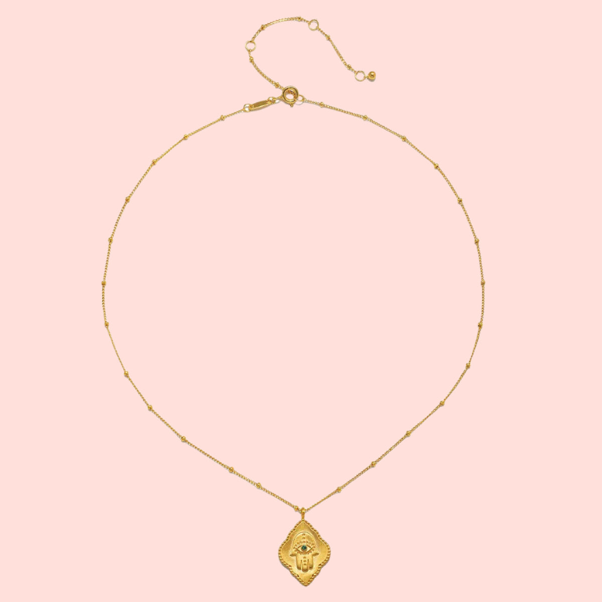 Elegant 16" Emerald Hamsa Pendant Necklace features a thin, beaded chain with a stylized hand pendant and engraved details. The adjustable 3" extension chain ensures the perfect fit.