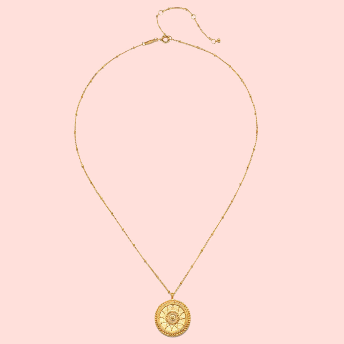The 18&quot; Sunburst Medallion Necklace features a gold plated, thin beaded chain and a round, textured sun-moon-star pendant with a central gemstone, shown on a plain white background.