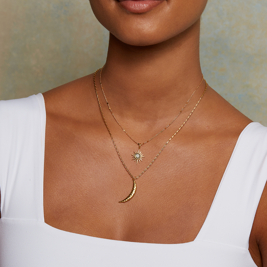 A woman wearing a white square-neck top and two gold necklaces: one is the 16&quot; Labradorite North Star Necklace layered with a sun pendant. Only her neck and shoulders are visible.