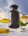 A black tea jar labeled "Air" sits among floating elements: a lemon slice, a teacup with lavender, a wine glass with tea and mint, all set against a cloudy sky background.