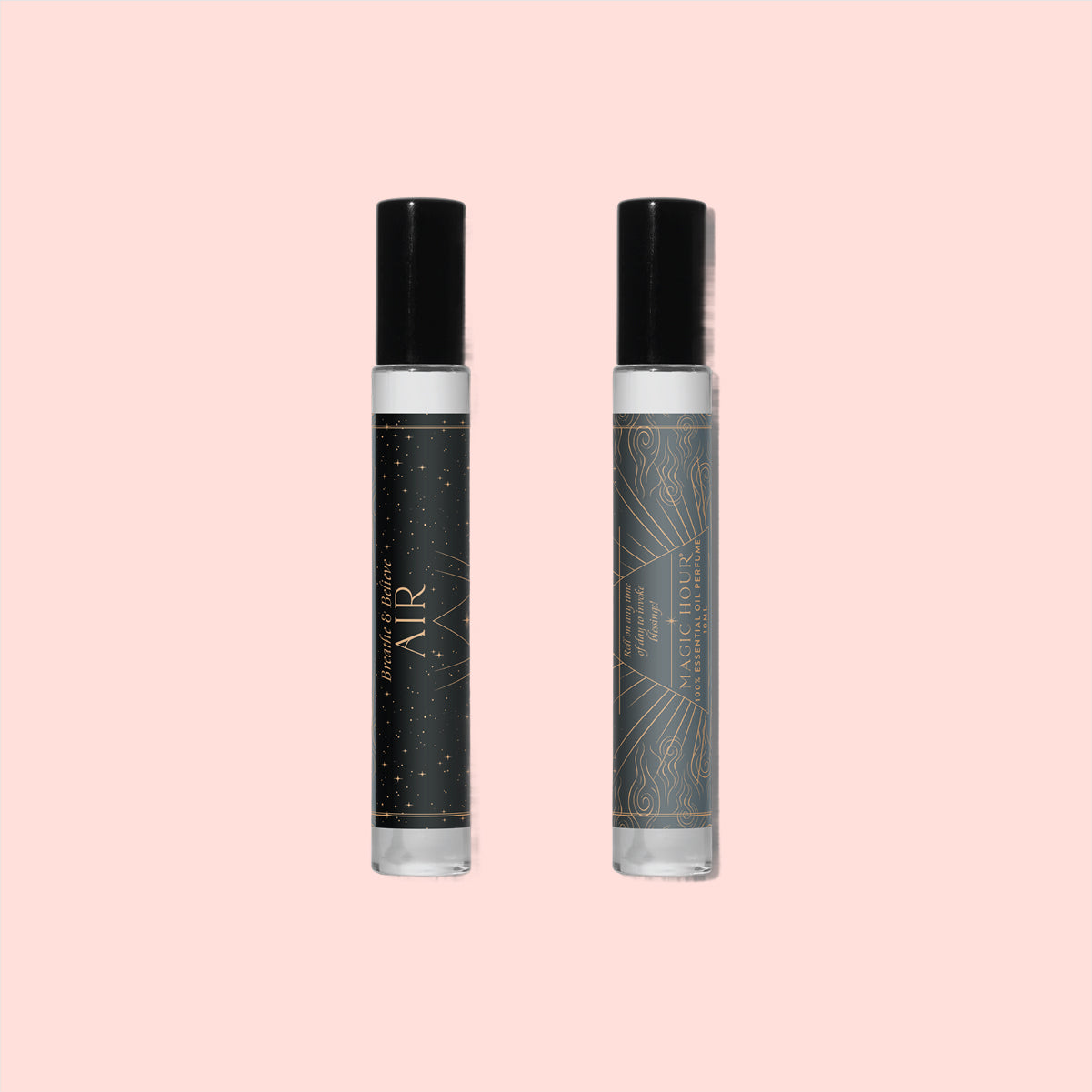 Two Air Essential Oil Perfume roller bottles with black caps rest on a light pink background. The left bottle features a dark label with gold stars; the right one has a grey label adorned with geometric gold patterns.