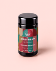 A black tea canister labeled “Campfire Breakfast: Golden Tipped Assam, Puerh & Lapsang Souchong Pine Smoked Connoisseur’s Cup for Nostalgic Mornings” sits on a pastel pink background. The eye-catching label features the phrases “Sip Curiously” and “Black Tea,” along with green, red, and tan design accents. This smoky blend’s inclusion of lapsang souchong makes it a bold and flavorful coffee alternative for those seeking an adventurous start to their day.