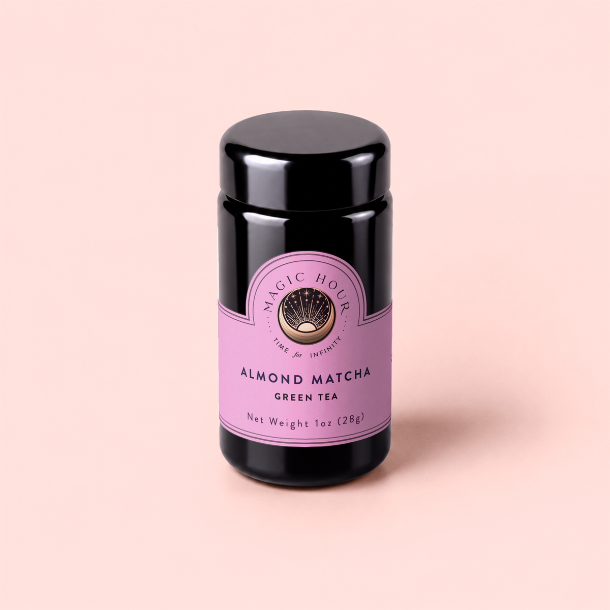 A black jar of Magic Hour Almond Matcha Green Tea for Joy with a purple label sits on a pale pink background. The label showcases the brand name, product name, and net weight of 1 oz (28g). This antioxidant-rich blend is crafted to help boost metabolism while delighting your senses.