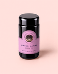 A black jar of Magic Hour Almond Matcha Green Tea for Joy with a purple label sits on a pale pink background. The label showcases the brand name, product name, and net weight of 1 oz (28g). This antioxidant-rich blend is crafted to help boost metabolism while delighting your senses.