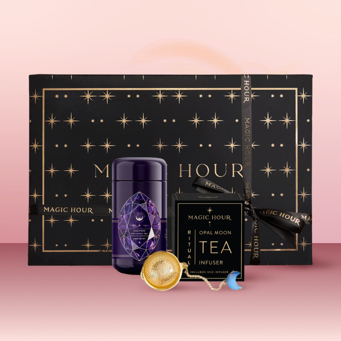 The Amethyst February Birthstone Mini Gift Set features a black and gold star-patterned Magic Hour gift box, a purple Amethyst Wellness Tea tin, an Opal Moon Ritual Tea Infuser, and a gold tea infuser ball on a pink surface.