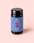 A black jar featuring a vibrant purple and blue label that reads “Magic Hour 444: Sachiel’s Prosperity Apple-Berry Herbal Tea with Butterfly Pea Flower and Blue Spirulina” sits against a light pink background, evoking the mystical energy of Angel Number 444 and the soothing qualities of Third Eye Chakra tea.