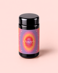 A black jar with a vibrant, radiant label reading “777: Celestial Messengers Dawn Pineapple Passionfruit Green Tea” rests on a pale pink background. The label—drawing inspiration from the uplifting essence of Archangel Gabriel tea—displays starburst patterns in pink, orange, and purple tones, inviting you to experience this spiritual awakening blend.