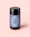 A black jar with a pastel, iridescent label reading “999: Adaptogenic Pineapple-Mint-Jasmine Herbal Tea” on a light pink background. The label features purple and blue geometric and starburst designs, evoking the energy of the crown chakra to inspire prophetic dreams and peaceful sleep.