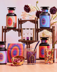 A vibrant display of Angel Tea Journey Subscription bottles, glasses, a gold bowl with rose petals, hourglasses, and decorative boxes on a wooden stand with flowers in the background evokes a spiritual tea ritual experience.